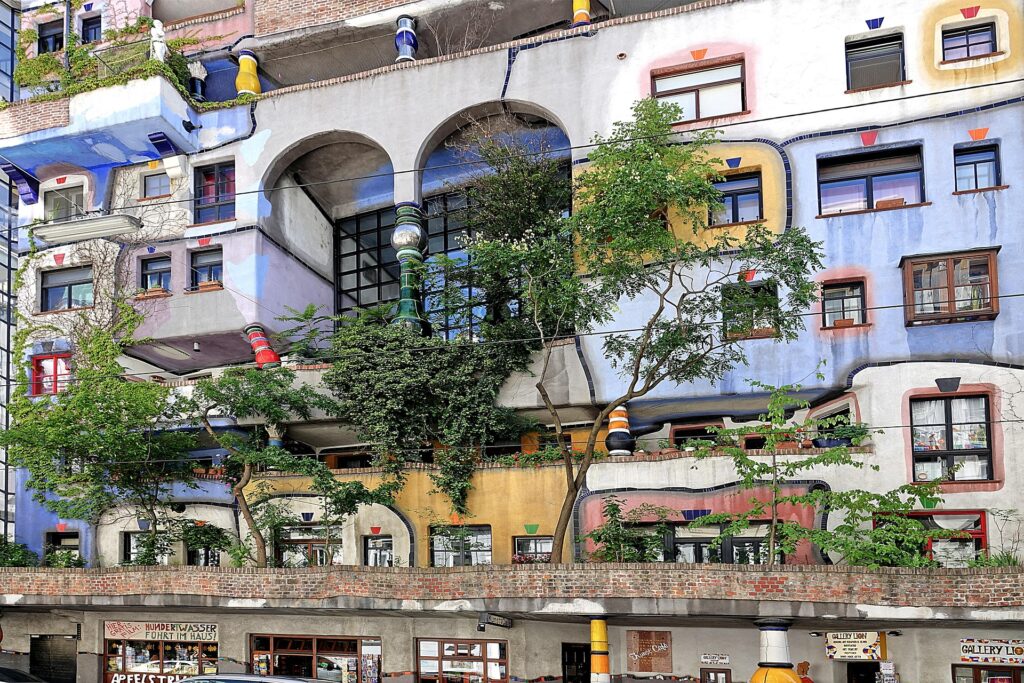 Hundertwasser-bygningen i Wien med farverige facader, skæve linjer, uens vinduer og træer, der vokser ud fra bygningen.